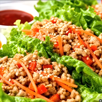 A platter of healthy Thai chicken lettuce wraps topped with matchstick carrots, red peppers, and green onions